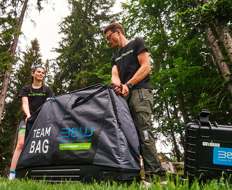 Zwei Mitglieder des Merida Teams mit großer B&W International Team Bag im Outdoor-Einsatz – robuste Transporttasche für Fahrradzubehör und Ausrüstung.