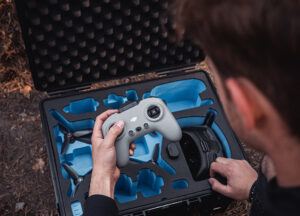 Person removes remote control from B&W International PP 326 drone case with custom-fit foam insert for safe transportation of drone and accessories.