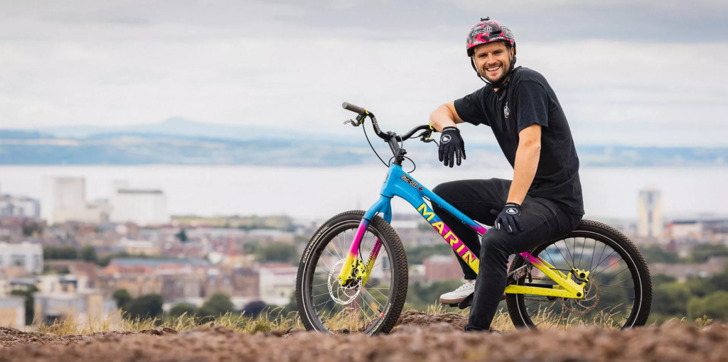 Duncan Shaw on a colorful trial bike in front of a city panorama, professional bike stunt rider in cooperation with B&W International.
