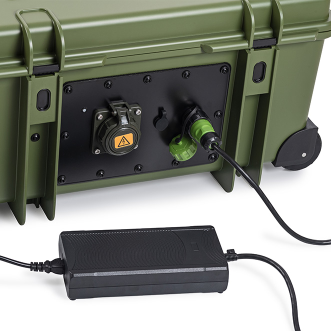 Bronze-grün B&W International Energiekoffer mit angeschlossenem Ladegerät am Technikmodul, robuste mobile Lösung für Energieversorgung im Einsatz.