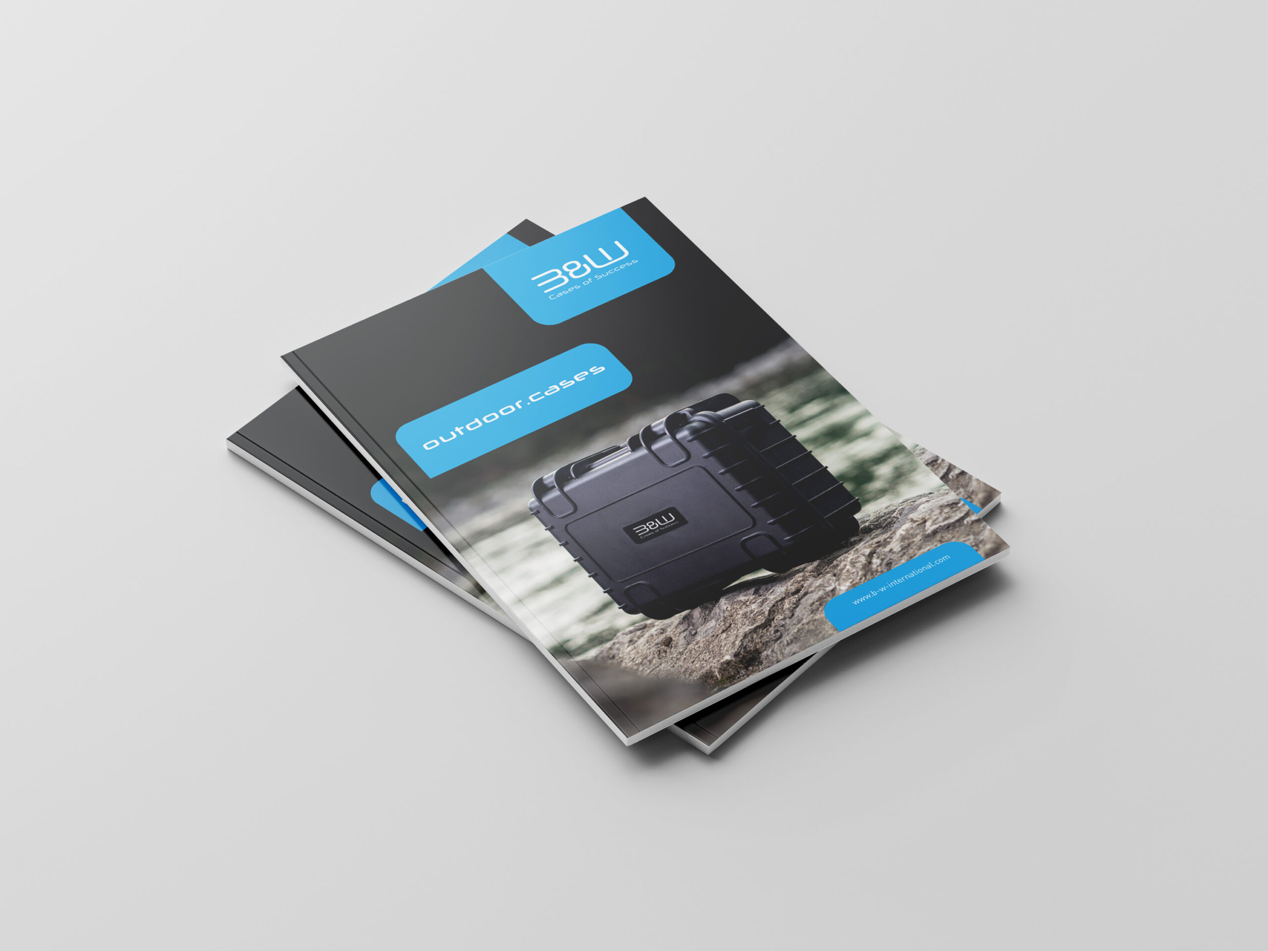 Stapel von Broschüren mit einem schwarzen Outdoor-Koffer auf einer felsigen Oberfläche, beschriftet mit Outdoor Cases und dem 3BW-Logo von B&W International.